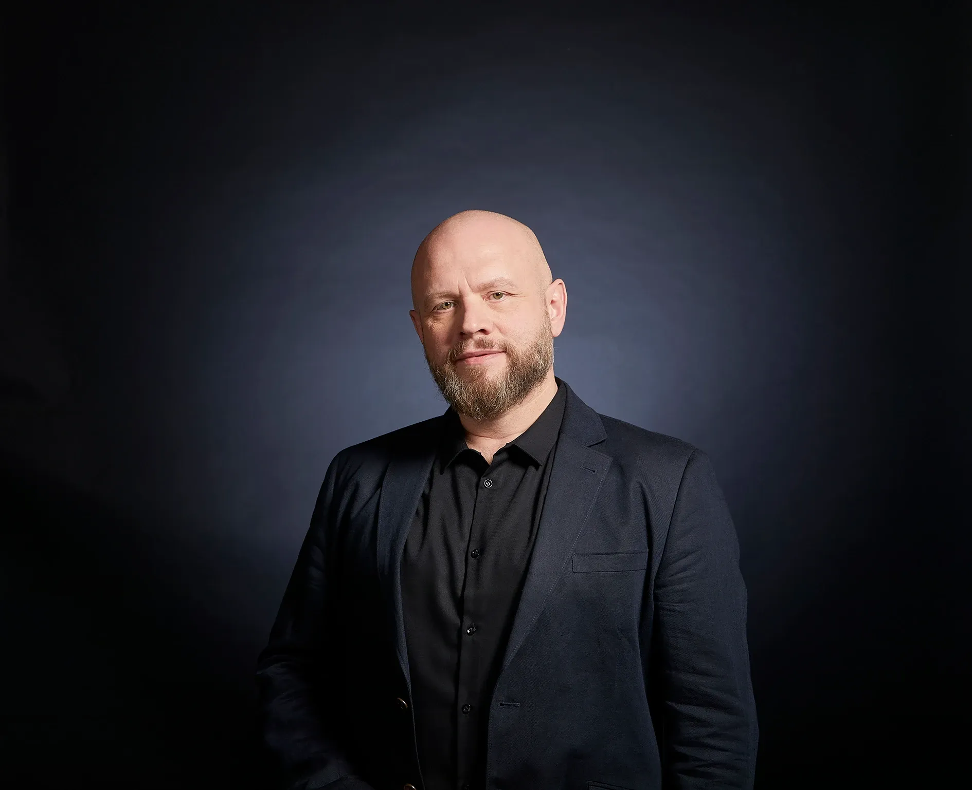 Alexander Golev smiling in a dark blazer against a dark blue background