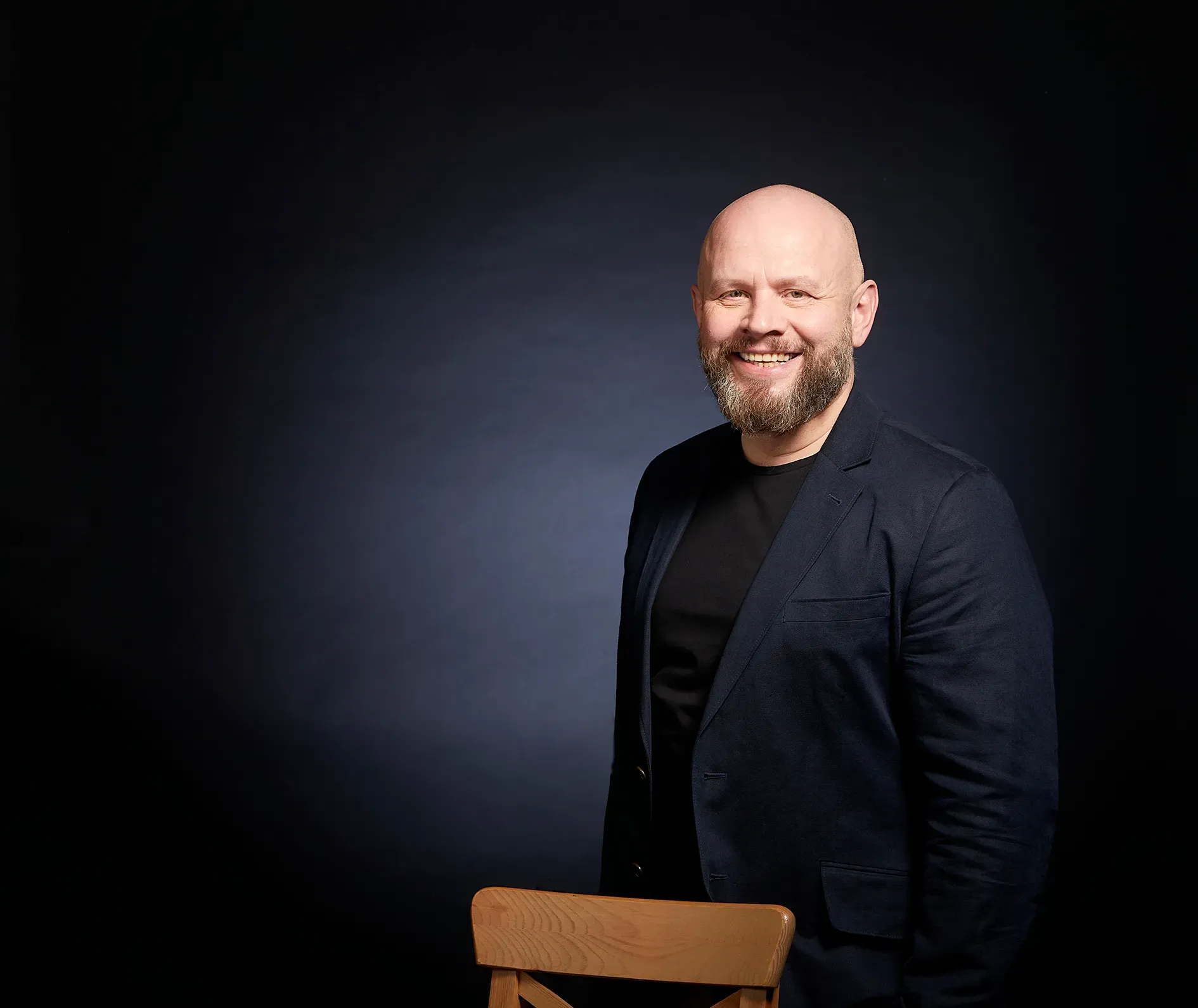 Alexander Golev in a dark blazer, smiling, photographed against a dark studio background