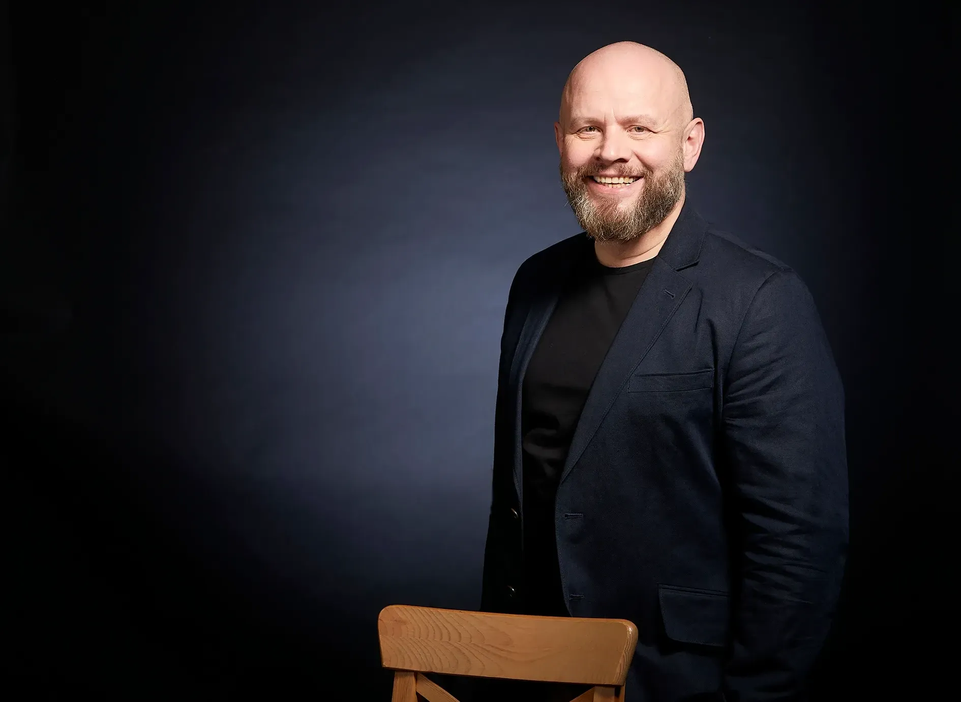 Alexander Golev in a dark blazer, smiling, photographed against a dark studio background